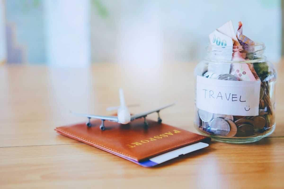Barattolo con risparmi, modellino aereo e passaporto poggiati su scrivania