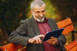 Uomo anziano su panchina che utilizza un tablet